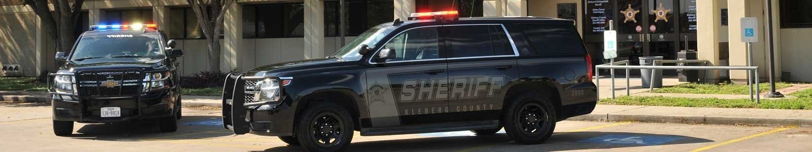 Two Kleberg County Sheriff’s Office patrol SUVs parked in front of the Adan Munoz Jr. Kleberg County Law Enforcement Center building with lights on